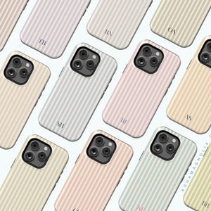 May include: A collection of pastel-colored phone cases with vertical striped patterns. Each case features a different color scheme, including pink, blue, and yellow, and is personalized with initials. The cases are designed for a smartphone.