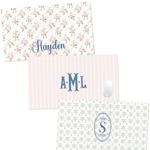 May include: Three rectangular mouse pads with decorative designs. One pad features a floral pattern with the name "Hayden" in blue script. Another has pink and white stripes with the initials "A.M.L." in blue. The third pad has a blue and white floral pattern with the letter "S".