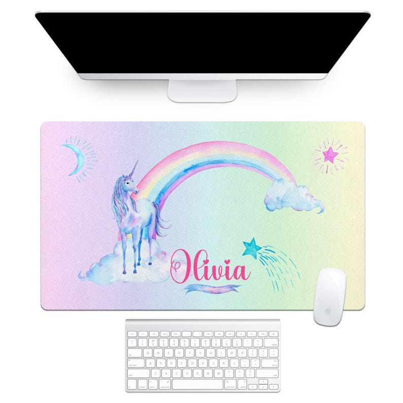 a desk pad with a pastel rainbow background, a unicorn on the left standing on clouds, a rainbow arc across the center and a shooting star on the right.  personalized with a name in a pink cursive font.  from the brand aqua magnolia.