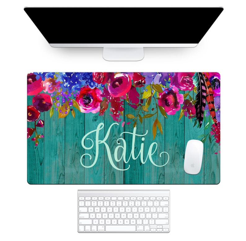image of a personalized desk pad with a teal wood-look background, colorful floral accents, feathers, and the name in white script. from the aqua magnolia brand.