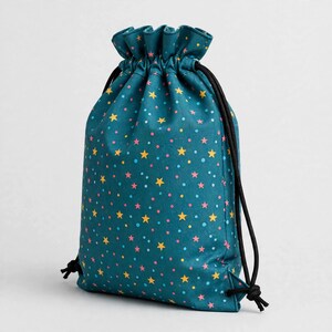 May include: A teal drawstring bag featuring a repeating pattern of small yellow stars, pink stars, and light blue dots. The bag has a gathered top closure secured by two black cord strings that extend from the sides to the top opening.