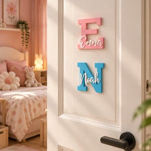 Könnte beinhalten: Zwei hölzerne Wandschilder an einer weißen Tür. Das obere Schild ist ein rosa Buchstabe E mit dem Namen Emma in weißer Schreibschrift. Das untere Schild ist ein blauer Buchstabe N mit dem Namen Noah in weißer Schreibschrift.
