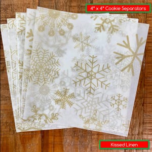 May include: Cookie separators, 4" x 4", with a white background and a gold snowflake pattern. The separators are made of Kissed Linen.