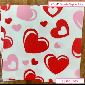 May include: White cookie separators, 4" x 4", printed with red and pink hearts of varying sizes. The separators are made of Kissed Linen and are designed to prevent cookies from sticking together.