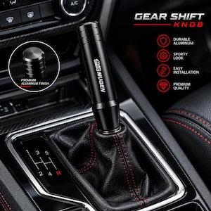 May include: A black cylindrical gear shift knob with the Mugen logo printed in white. The knob features a premium aluminium finish and is installed on a black leather gear shift boot with red stitching, positioned next to a manual gear pattern.