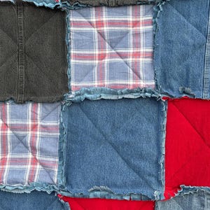 May include: Close-up of a patchwork quilt with squares of denim, red, and plaid fabric. The quilt has a textured appearance with visible stitching and frayed edges. The color palette includes shades of blue, red, and gray.