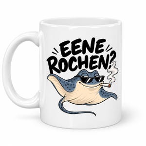Op de afbeelding: Een witte keramische mok met een cartoonillustratie van een blauwe en crèmekleurige rog die een zwarte zonnebril draagt en een sigaret rookt. Boven de rog staat de zwarte tekst EENE ROCHEN? met een klein wolkje rook dat omhoog stijgt.