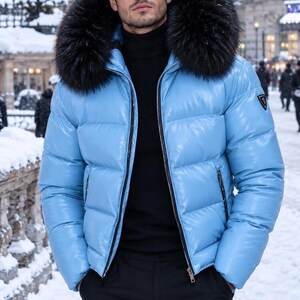 May include: A glossy light blue puffer jacket featuring a large, dark faux fur-trimmed hood, a full-length front zip, and two zipped side pockets. The jacket is worn over a black turtleneck jumper and black trousers in a snowy setting.