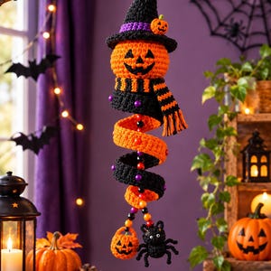 Può includere: Una decorazione all'uncinetto da appendere raffigurante una testa di zucca con un cappello da strega nero e un piccolo dettaglio a forma di zucca. Sotto la testa c'è una sciarpa a righe arancioni e nere e un corpo a spirale con perline.