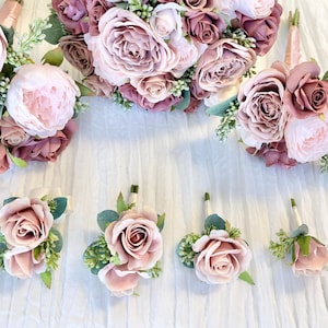 May include: A set of five bouquets of artificial flowers in shades of pink and mauve. The bouquets are arranged in a row on a white fabric background. The largest bouquet is in the center, with two smaller bouquets on either side, and two very small bouquets at the ends.