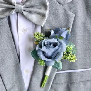 May include: A gray suit jacket with a silver bow tie and a blue rose boutonniere.