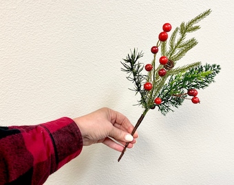 May include: A sprig of artificial greenery with red berries and a small brown pine cone.