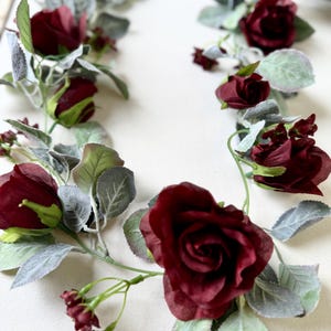 May include: A burgundy floral garland with faux roses and greenery. The garland is perfect for adding a touch of elegance to any space.