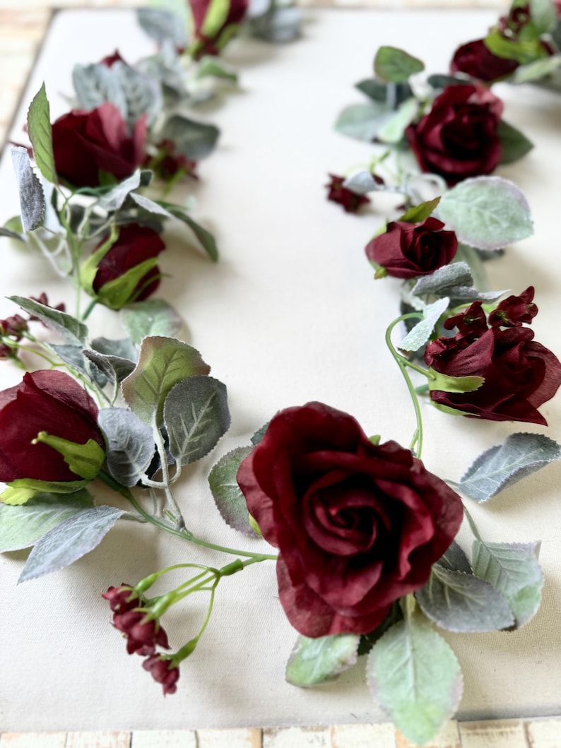 May include: A burgundy floral garland with faux roses and greenery. The garland is perfect for adding a touch of elegance to any space.