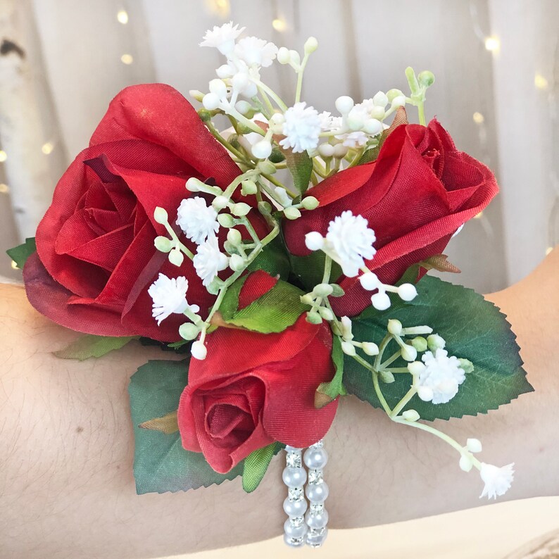 May include: A red rose wrist corsage with white baby's breath and pearl accents.