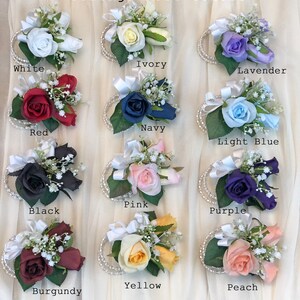 May include: Corsage Rose Colors: A collection of 12 corsages with different colored roses, including white, ivory, lavender, navy, red, light blue, pink, black, purple, yellow, peach, and burgundy.