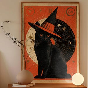 May include: A rectangular framed wall art print featuring a black cat wearing an orange and black witch hat. The background displays a large black circle with white stars and lines against a textured orange backdrop with gold accents.