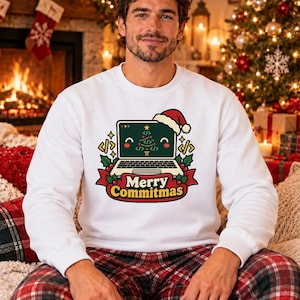 Könnte beinhalten: Ein weißes Langarm-Sweatshirt mit einer Grafik eines Laptops, der eine Weihnachtsmütze trägt. Auf dem Bildschirm ist ein Weihnachtsbaum aus Codesymbolen zu sehen. Unter dem Laptop befindet sich ein rotes Banner mit dem Text Merry Commitmas.