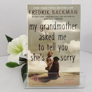 May include: A paperback book titled My Grandmother Asked Me to Tell You She's Sorry by Fredrik Backman. The cover features a child standing next to a large black dog against a cloudy sky. The text includes New York Times Bestseller and A Novel.