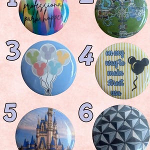 May include: Six circular pin-back buttons featuring various designs: a watercolor background with the text 'professional park hopper', a park map, pastel Mickey-shaped balloons on a blue background, yellow stripes with the text 'on my way to main street usa', a castle, and a geometric gray pattern.