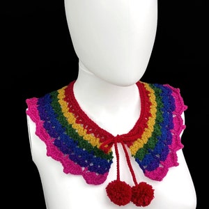Può includere: Un colletto a uncinetto arcobaleno con bordo a scalare e due pompon rossi legati sul retro.