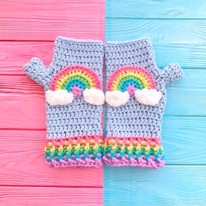 May include: A pair of blue crocheted fingerless gloves with rainbow and cloud designs. The gloves are on a pink and blue wooden background.