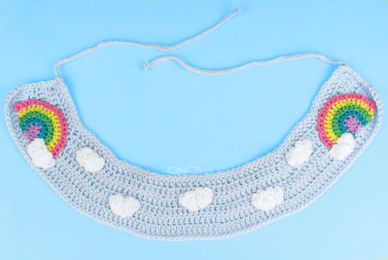Pu&ograve; includere: Un cerchietto in crochet blu chiaro con due motivi arcobaleno e nuvole. Il cerchietto ha una chiusura a nodo.