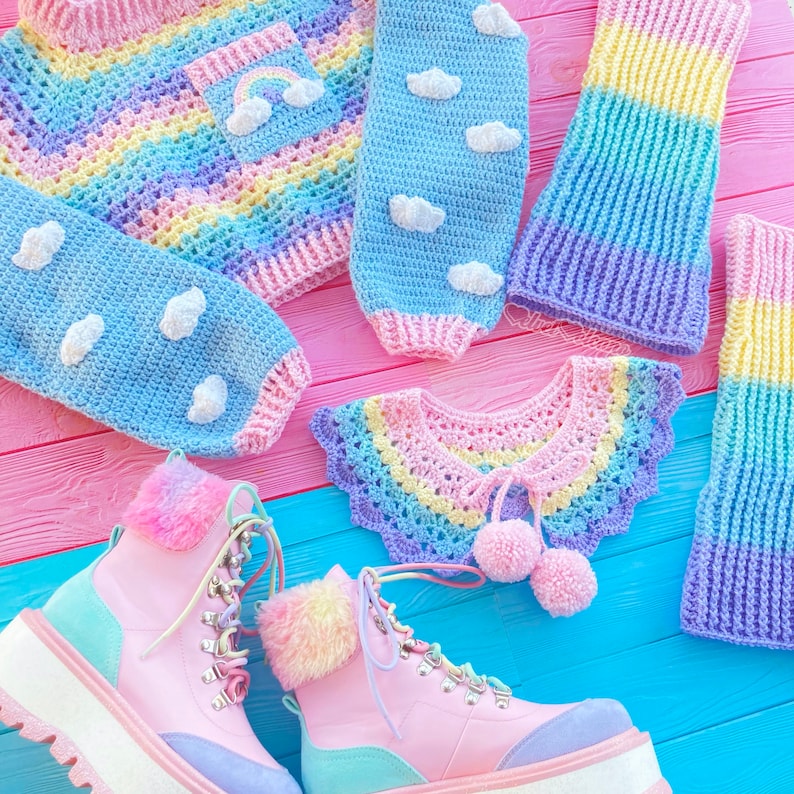 May include: A set of colorful crocheted clothing items, including a rainbow striped sweater, a blue cloud-patterned sweater, a rainbow striped collar, and a pair of pink and blue boots.
