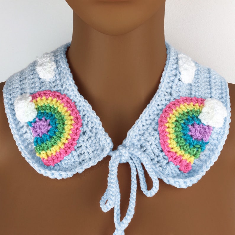 Pu&ograve; includere: Un colletto in crochet azzurro con un design arcobaleno e nuvola bianca. Il colletto ha una chiusura a cravatta.