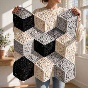 May include: A crochet blanket featuring a geometric 3D cube pattern created with individual floral motif squares. The design uses a color palette of black, light gray, and cream yarn, arranged to form an optical illusion of stacked cubes.