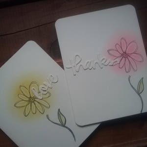 Two ivory cards show an outlined flower, stem and single leaf.  One has yellow sponged background.  The other has pink sponging.  One has the die-cut word "love" on the front.  The other has "thanks."