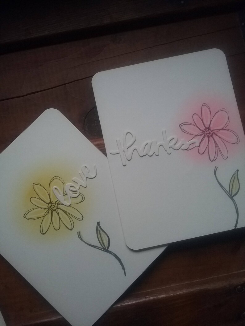 Two ivory cards show an outlined flower, stem and single leaf.  One has yellow sponged background.  The other has pink sponging.  One has the die-cut word "love" on the front.  The other has "thanks."