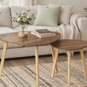 May include: A set of two nesting coffee tables featuring dark brown, triangular-shaped wooden tops with rounded edges and light-colored, tapered wooden legs. The tables are positioned together, with the smaller table partially tucked under the larger one.