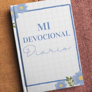 May include: A hardback journal with a white grid background, a blue border, and blue flower illustrations in the top-left and bottom-right corners. The text on the cover reads MI DEVOCIONAL Diario in blue, serif, and script fonts.