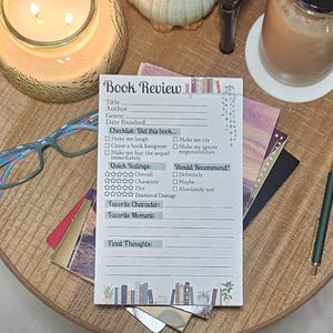 May include: A rectangular book review notepad featuring printed fields for title, author, genre, and date finished, along with a checklist, rating stars, and sections for favorite character, moment, and final thoughts, decorated with small book illustrations.