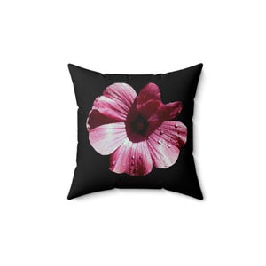 Könnte beinhalten: Ein quadratisches Dekokissen mit einfarbig schwarzem Hintergrund und einer großen, mittig platzierten rosa Blume. Die Blütenblätter weisen eine sichtbare Textur auf und sind mit kleinen, klaren Wassertropfen bedeckt, was ein kontrastreiches botanisches Design ergibt.