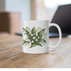 May include: A white ceramic mug featuring a botanical illustration of lily of the valley flowers with small white bell-shaped blossoms and green leaves centered on the front. The mug has a smooth finish and a curved handle on the right side.