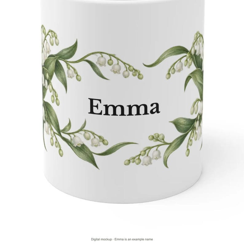 May include: A white ceramic mug featuring a botanical illustration of lily of the valley flowers with green leaves and white bell-shaped blossoms. The name Emma is printed in a black serif font in the center between the floral arrangements.