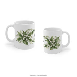 May include: Two white ceramic mugs displayed side by side, each featuring a botanical illustration of lily of the valley flowers with green leaves and small white bell-shaped blossoms. The mugs have a standard cylindrical shape and a handle.