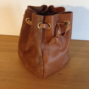 Peut inclure: Un petit sac à cordon en cuir marron avec des accents en daim et des œillets en laiton.