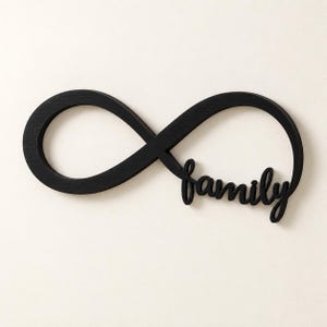 Könnte beinhalten: Eine schwarze Wanddekoration in Form eines Unendlichkeitssymbols, bei der das Wort family in Schreibschrift in die untere rechte Schleife des Symbols integriert ist. Das Objekt hat eine glatte, matte Oberfläche und ein fließendes Design.