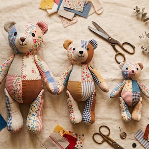 May include: Three handmade teddy bears crafted from various fabric patches including floral, gingham, and corduroy patterns. The bears feature dark button eyes and stitched noses. Two pairs of metal scissors and fabric scraps are scattered nearby.