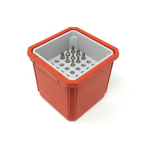May include: A square, orange storage container with a light grey insert featuring a grid of circular holes. Several metallic screwdriver bits of varying shapes and sizes are inserted into the centre of the grid, standing upright within the container.