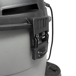 May include: A grey and black wet-dry vacuum cleaner featuring a prominent black plastic locking latch on the side. The upper housing is dark charcoal, while the lower canister is a lighter grey, with a black power cord visible on the right side.