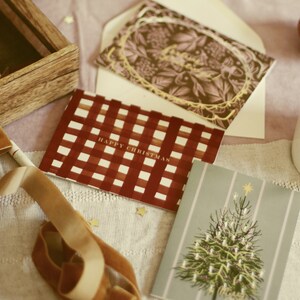 May include: Christmas cards with festive designs. One card features a red and white checkered pattern with "HAPPY CHRISTMAS" text. Another card has a Christmas tree illustration. A wooden box and a velvet ribbon are also present.