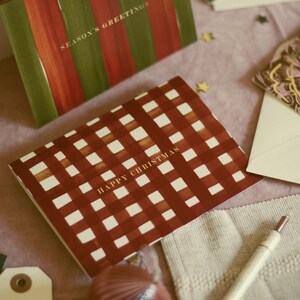 May include: Greeting cards with festive designs. One card features red and green stripes with "SEASON'S GREETINGS." Another card has a red and white checkered pattern with "HAPPY CHRISTMAS." Other cards and decorative elements are also visible.