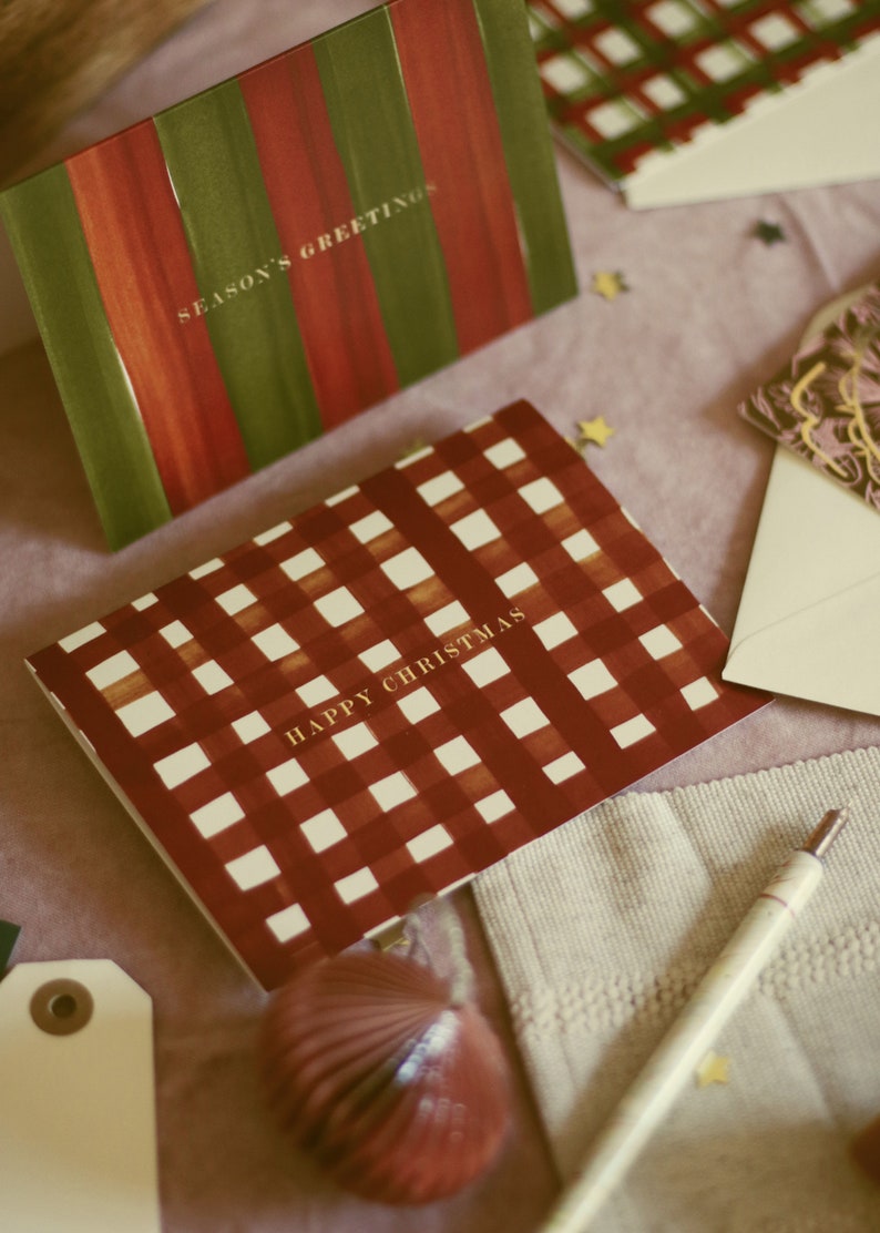 May include: Greeting cards with festive designs. One card features red and green stripes with "SEASON'S GREETINGS." Another card has a red and white checkered pattern with "HAPPY CHRISTMAS." Other cards and decorative elements are also visible.