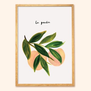 May include: Framed art print with a watercolour illustration of peaches and green leaves. The handwritten text "la peche" is in black. The print is set in a natural wood frame, suitable for home decor and wall art.