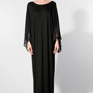 Puede incluir: Vestido negro largo con escote redondo y mangas anchas. Los pu&ntilde;os de las mangas tienen detalles de encaje. El vestido est&aacute; hecho de una tela fluida, ideal para eventos especiales o de noche.