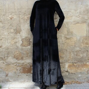 May include: A long black velvet dress with a mock neck and long sleeves. The dress has a loose fit and falls to the ankles.